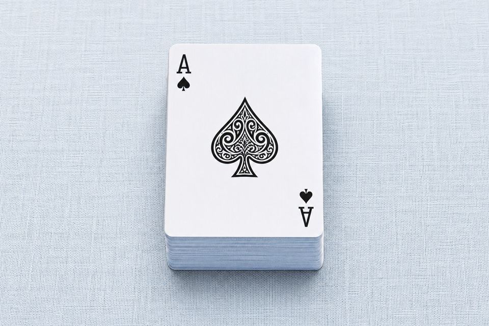 浅蓝亚麻桌布上整齐叠放的一副扑克牌，最上方是黑桃A
